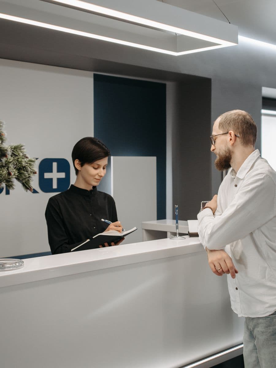 A patient speaking with staff at a medical practice front desk